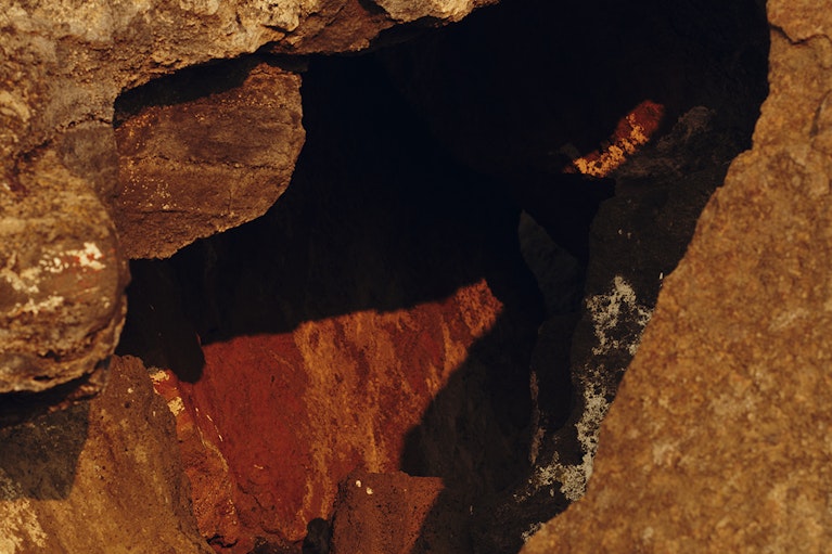 A close-up photograph of a small cave in rock tinted orange and red at Fort Rock in Oregon.
